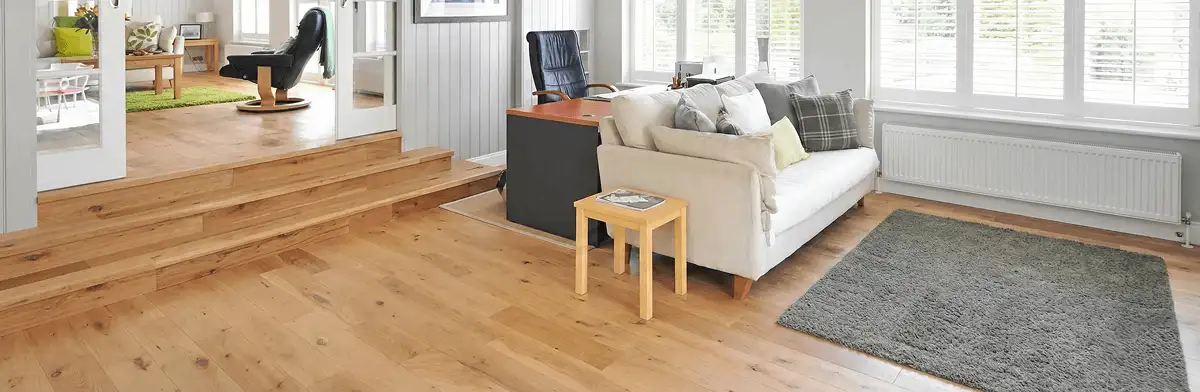 A modern living room with professionally installed laminate flooring, a beige sofa, a small side table, a gray rug, and large windows with white shutters in Rockford, IL